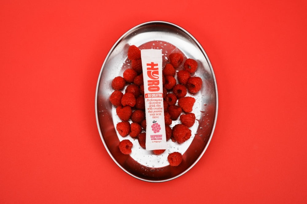 Hyro Raspberry Electrolytes + Creatine stick on a tray of fresh raspberries