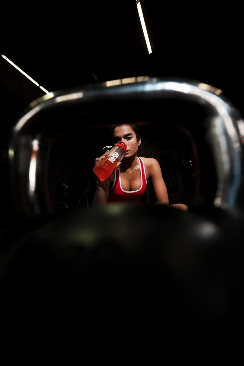Woman drinking a Hyro Electrolytes + Creatine bottle in a dramatically lit gym
