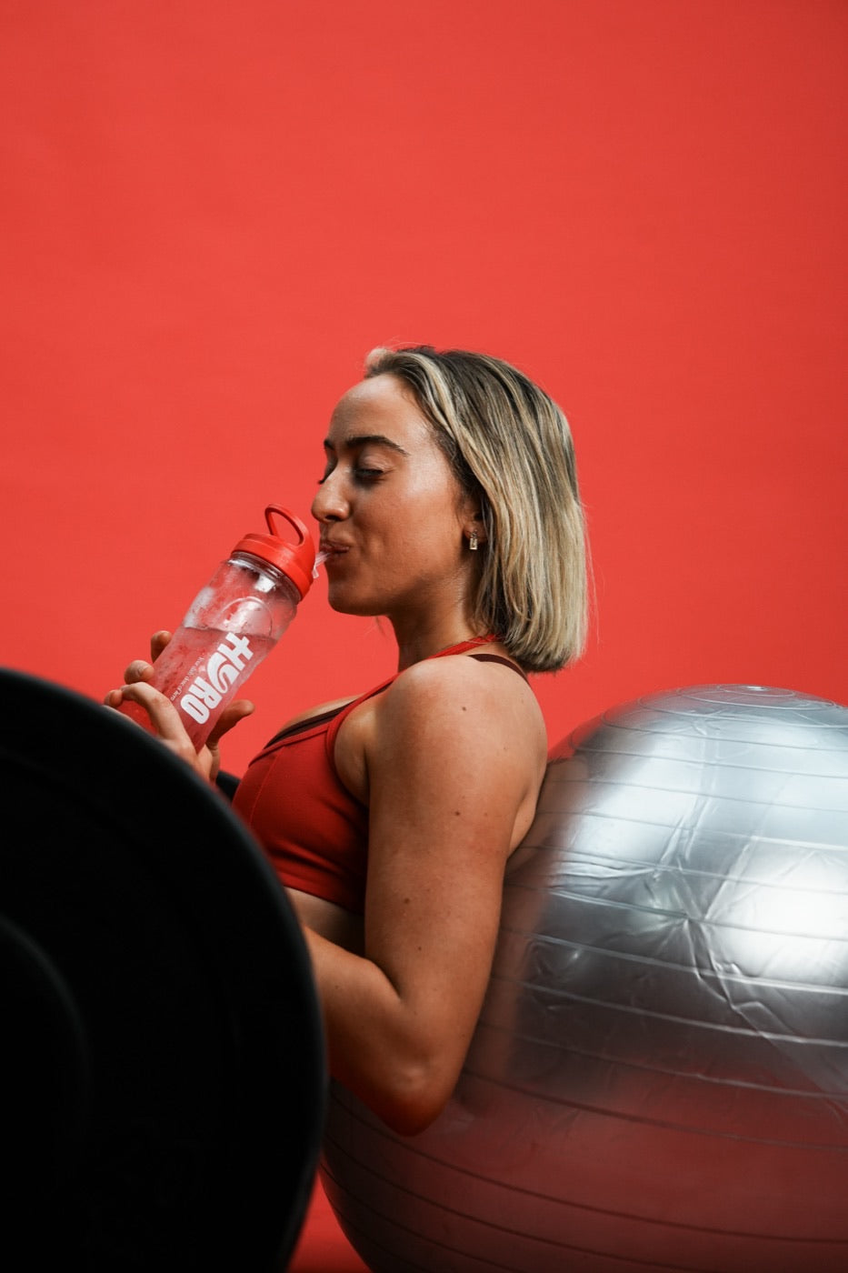 Woman in red activewear pouring a Hyro raspberry stick into a bottle of water